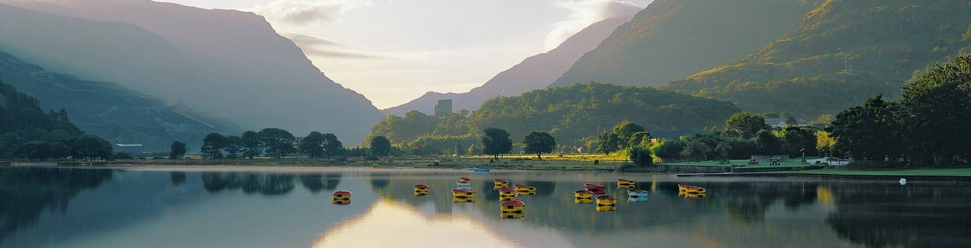 A peaceful view of Llyn Padarn lake with calm waters reflecting the surrounding mountains.