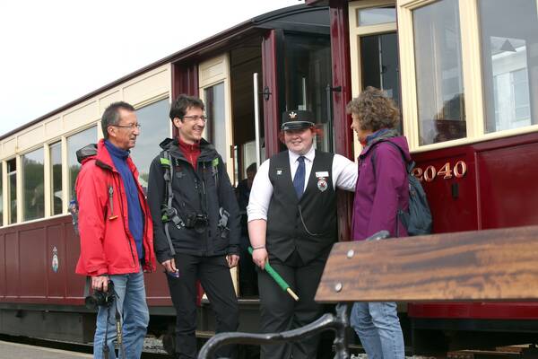 A Welsh Highland Railway conductor standing at a carriage door, chatting with visitors before their train journey.
