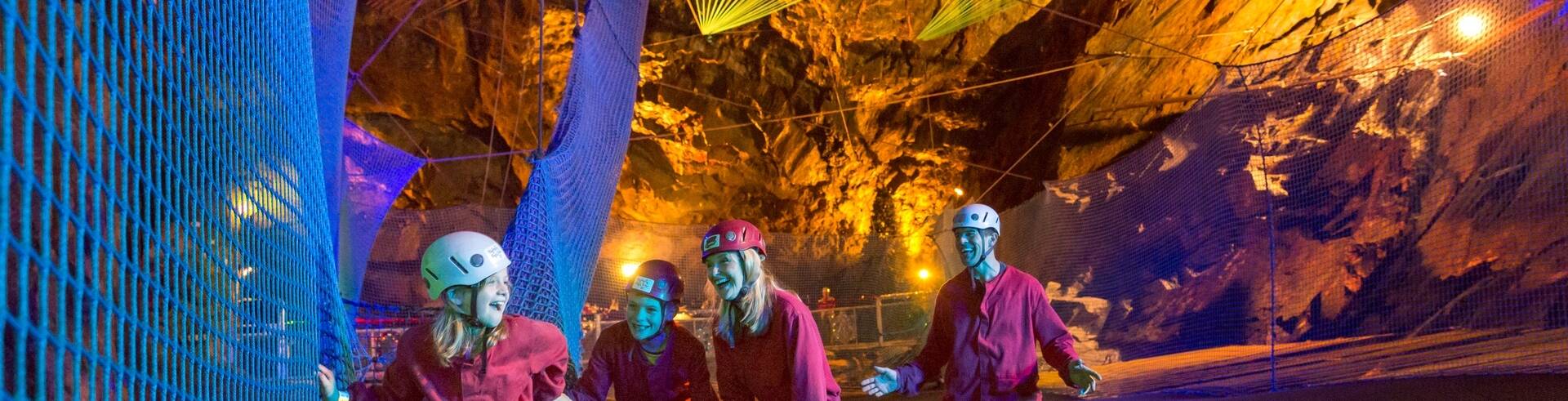 Visitors wearing helmets and overalls exploring illuminated underground caverns at Zip World near Llanberis.