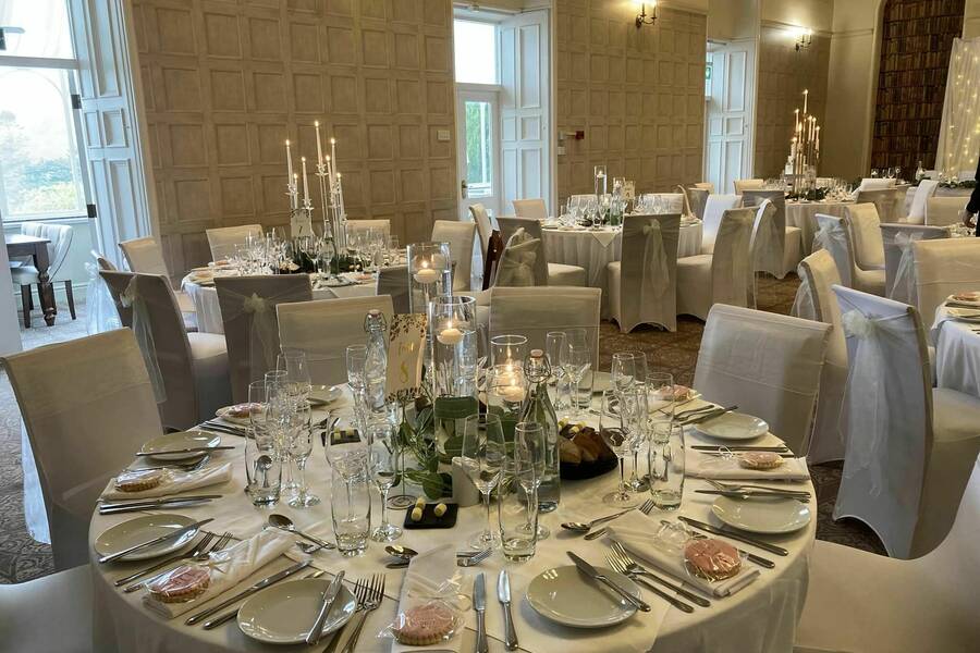 Elegant wedding tables set with white linen, candles, glassware and place settings in the Royal Victoria Hotel’s historic dining room.