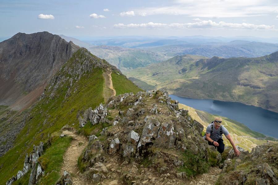 Hiker scrambling along the narrow Crib Goch ridge with steep drops and mountain views over Snowdonia.