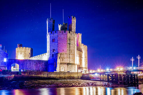 Illuminated night view of Caernarfon Castle beside the River Seiont in North Wales