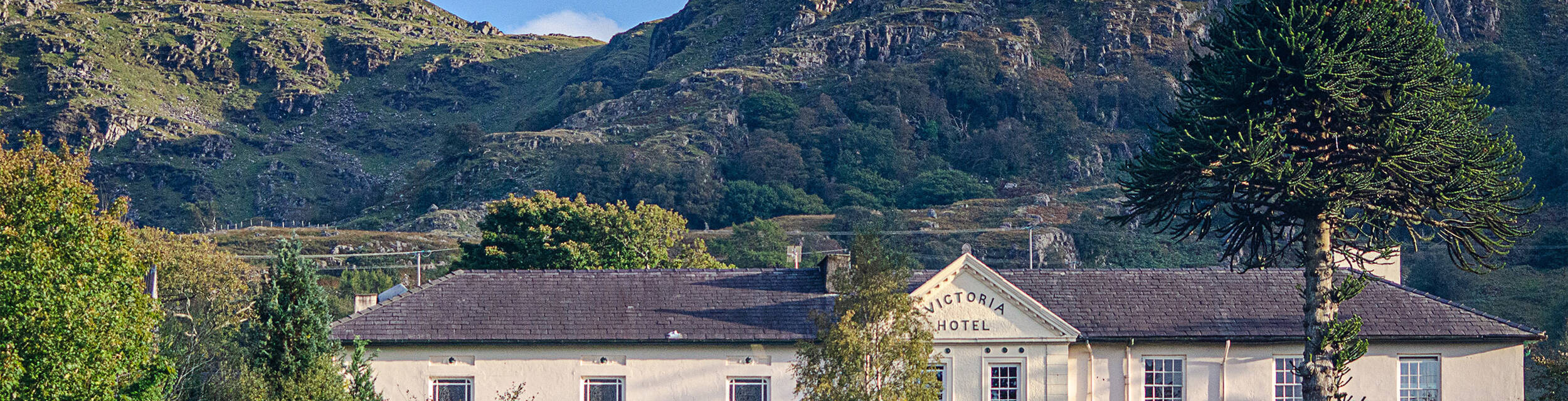 A view of the Royal Victoria Hotel in Snowdonia surrounded by lush gardens and mountains.