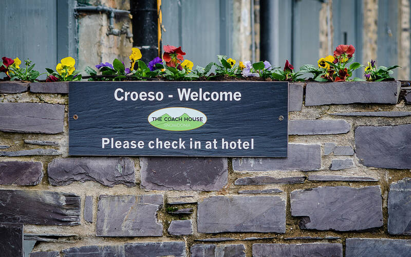Welcome sign for The Coach House at the Royal Victoria Hotel in Llanberis, with bilingual “Croeso – Welcome” text and colourful flowers above a slate wall.